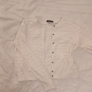 Vit stickad kofta från Zara - Säljer en söt vit stickad kofta från Kapphal med ett fint hålmönster. Koftan har långa ärmar och knappar framtill. 