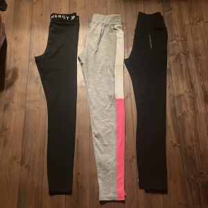 Tre par leggings i olika färger - Säljer tre par leggings. Ett par svarta med 'Energy' tryckt på midjan xs, ett par grå med vita och rosa sidopaneler158/164, och ett par helsvarta xs. Perfekta för träning eller en avslappnad dag. Priset kan diskuteras!