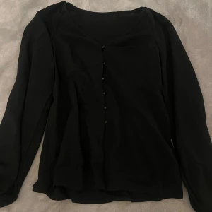Svart blus med knappar - Elegant svart blus med långa ärmar och knappar framtill. Perfekt för en stilren look.