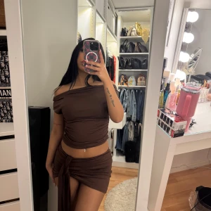 Brun offshoulder klänning - Snygg brun offshoulder klänning med en tight passform. Klänningen har en knytbar detalj i midjan och är kort i modellen. Perfekt för en trendig look!