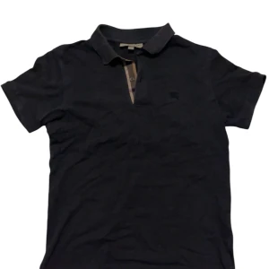 Svart pikétröja från Burberry - Säljer en stilren svart pikétröja från Burberry. Tröjan är tillverkad i 100% bomull och har en klassisk krage med knappdetaljer. Perfekt för en avslappnad men ändå elegant look. PRIS EJ HUGGET I STEN!