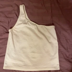 Vit oneshoulder topp från Gina Tricot - Säljer en stilren vit oneshoulder topp från Gina Tricot. Toppen är ribbad och har en modern design som passar perfekt för varmare dagar. Perfekt för att skapa en trendig look!