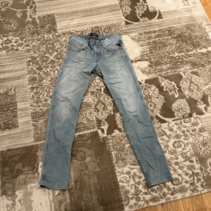 Ljusblå jeansbyxor från Replay  - Snygga ljusblå jeansbyxor med en klassisk femficksdesign. De har en rak passform och är perfekta för en avslappnad stil. Byxorna har en dragkedja och knapp framtill.