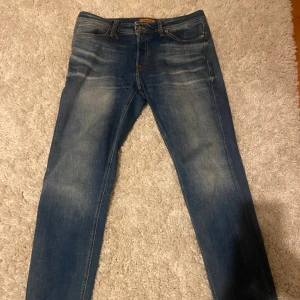 Blå jeans från Jack & Jones - Snygga blå jeans från Jack & Jones med en klassisk femficksdesign. De har en lätt tvättad look och orange sömmar som ger en cool kontrast. Perfekta för en avslappnad stil.