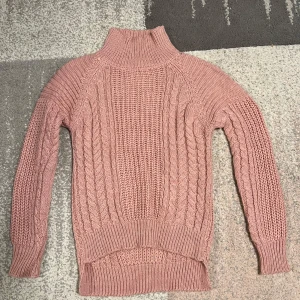 Rosa stickad polotröja - Säljer en mysig rosa stickad polotröja med kabelstickat mönster. Tröjan har långa ärmar och en hög polokrage som håller dig varm under kyliga dagar. Perfekt för höst och vinter!