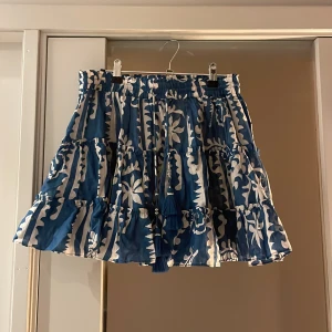 Blå och vit kjol från Zara - Snygg blå och vit kjol från Zara med ett blommigt mönster. Kjolen har en volangdetalj och en elastisk midja för en bekväm passform. Nypris: 349kr