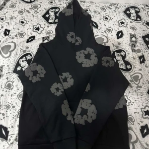 Svårt denim tears hoodie - Säljer en svart hoodie med ett unikt grått mönster. Tröjan har en klassisk huva och en stor ficka framtill. Perfekt för en avslappnad stil.