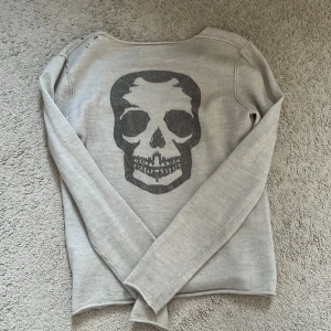 Grå tröja med dödskalle från Zadig & Voltaire - En sååå snygg gråbeige tröja från Zadig & Voltaire med en stor dödskalle på ryggen. Tröjan har en v-ringad hals och långa ärmar. Köpte från Sellpy där det står storlek M men passar mig som har xs/s så mindre i storlek💕några små hål på ena axeln som redan var där når jag köpte den (sista bilderna)❣️❣️