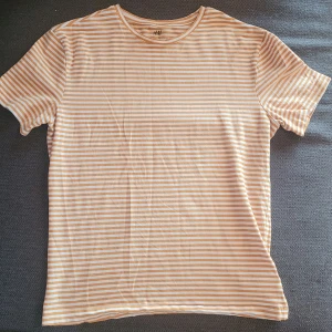 Randig t-shirt från H&M - Säljer en stilren randig t-shirt från H&M i slim fit. T-shirten har en klassisk rund hals och korta ärmar. Perfekt för en avslappnad look.