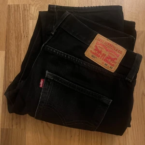 Svarta jeans från Levi's 501 - Snygga svarta Levi's 501 jeans i klassisk design. De har en rak passform och är tillverkade i slitstarkt denim. Perfekta för en stilren look med den ikoniska Levi's-lappen på baksidan.                        Storlek:                                                                                W:30 L:32