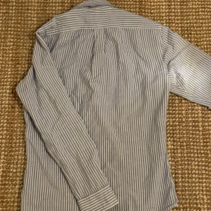 Randig skjorta från Polo Ralph Lauren - Snygg randig skjorta från Ralph Lauren i slim fit. Skjortan är blå och vit med långa ärmar och knappar framtill. Perfekt för en stilren look.