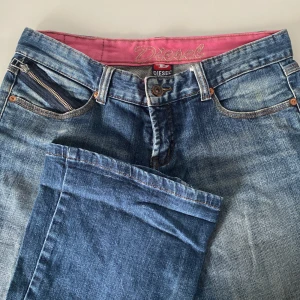 Blå jeansshorts från Diesel - Snygga blå jeansshorts från Diesel med en cool slitningseffekt. De har en klassisk femficksdesign och en dragkedja fram. Insidan är fodrad med en rosa detalj som ger en extra touch. Perfekta för vardag och festligare kvällar!
