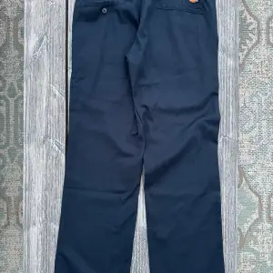 Snygga mörkblå byxor från Dickies i modellen Slim Straight. De har en klassisk design med dragkedja och knapp framtill. 