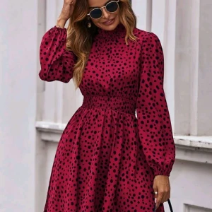 Vinröd prickig klänning - Snygg vinröd klänning med svarta prickar och hög hals. Klänningen har långa ärmar och en smockdetalj i midjan som ger en fin passform. Perfekt för en chic look!