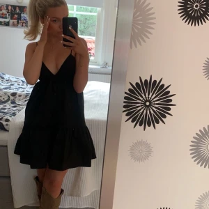 Svart kort klänning med knytband Zara - Snygg svart klänning med v-ringning och knytband i ryggen. Den har en volangdetalj i nederkanten som ger en fin touch. Perfekt för en somrig look! Banden går att justera