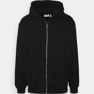 Svart hoodie från Weekday - Säljer en stilren svart hoodie från Weekday. Den har en dragkedja framtill och en klassisk huva med dragsko. Perfekt för en avslappnad look. Stor ficka framtill för extra bekvämlighet.