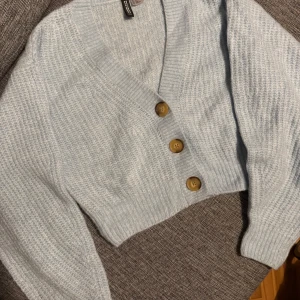 Ljusblå stickad kofta med knappar - Mysig ljusblå stickad kofta från H&M med stora träknappar framtill. Koftan har en croppad passform och långa ärmar med ribbade muddar. Perfekt för kyliga dagar!