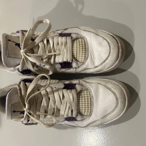 Jordan 4 metallic purple - Säljer ett par klassiska vita Nike Air Jordans med lila detaljer. Skorna har snörning och en ikonisk design med Jumpman-loggan på baksidan. Perfekta för dig som älskar retrostil och vill ha något unikt i garderoben. Skick är 8/10 och priset är diskuterbart.