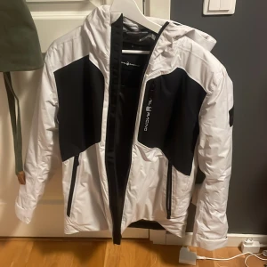 Vit och svart jacka från Sail Racing - Säljer en stilren vit och svart jacka från sail racing . Jackan har en dragkedja framtill och praktiska fickor med dragkedjor. Den är långärmad och har en justerbar huva. Perfekt för kyligare dagar. Den är köpt för 4000 på Johlens och använd 4 gånger. Priset är inte hugget i 🪨.