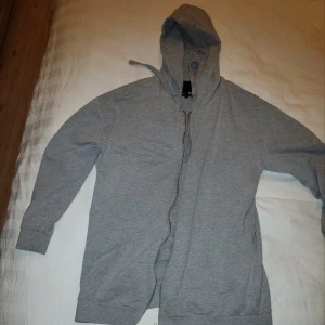 Grå hoodie med dragkedja - Säljer en bekväm grå hoodie med dragkedja och huva. Perfekt för en avslappnad stil. Tröjan har långa ärmar och är tillverkad i ett mjukt material.