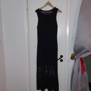 Svart långklänning med stickade detaljer från Lindex - Elegant svart långklänning med stickade detaljer i nederdelen. Klänningen är ärmlös och har en stilren design som passar perfekt för festliga tillfällen. Den stickade strukturen ger en unik touch och gör den både bekväm och chic.