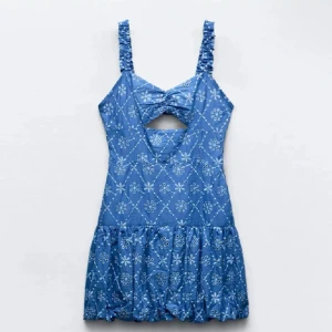 Blå klänning Zara - Charmig blå klänning med blommigt mönster och volangdetaljer. Den har en unik öppen rygg och knytning framtill. Axelbanden är breda och klänningen har en kort längd som ger en somrig känsla.