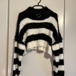 Randig fluffig tröja från Deviants - Säljer en supermjuk och fluffig tröja från Deviants i svart och vitt. Tröjan har ett randigt mönster och ett litet hjärta broderat vid halsen. Perfekt för att hålla sig varm och stilren. 🖤🤍