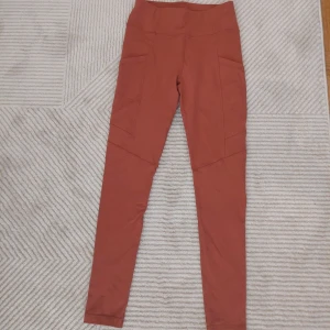 Rostfärgade leggings från SOC - Snygga rostfärgade leggings från SOC med hög midja och praktiska sidofickor. Perfekta för träning eller en aktiv vardag. Materialet är stretchigt och andas bra, vilket gör dem bekväma att bära under längre perioder.