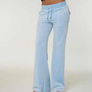 Ljusblå mjukisbyxor från Juicy Couture - Snygga ljusblå mjukisbyxor från Juicy Couture med breda ben och praktiska fickor både fram och bak. Byxorna har en bekväm dragsko i midjan och är perfekta för en avslappnad stil. Materialet är mjukt och skönt. Mettalbitarna från snörena har ramlat av men ingenting man tänker på.