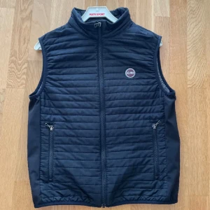 Colmar väst - Säljer en stilren svart väst från Colmar med dragkedja framtill och två praktiska fickor med dragkedjor. Västen har en quiltad design och en rund Colmar-logga på bröstet. Perfekt för lager-på-lager under kyligare dagar eller till vardagen. Använd 1 sommar så bra skick köpt på colmars egna hemsida.