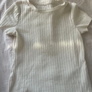 Vit ribbad t-shirt - Säljer en stilren vit ribbad t-shirt med korta ärmar. Perfekt för en enkel och avslappnad look. Passar bra till jeans eller shorts för en casual stil.