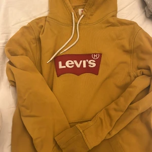 Gul hoodie från Levi's - Säljer en snygg gul hoodie från Levi's med det klassiska logotypen på bröstet. Tröjan har en justerbar huva med vita snören och långa ärmar. Perfekt för en avslappnad stil.