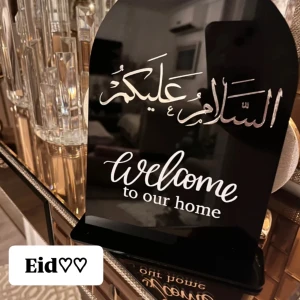 Svart dekorativ skylt med Eid Mubarak och välkomsthälsning - Elegant svart skylt med texten 'Eid Mubarak' i guld och 'Welcome to our home' i vitt. Perfekt för att dekorera hemmet under Eid. Skylten har en stilren design med en halvmåne och stjärna upptill.