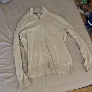 Säljer en stilren beige tröja från Jack & Jones med dragkedja vid halsen. Tröjan har långa ärmar och ribbade muddar vid ärmslut och nederkant. Perfekt för en avslappnad look.