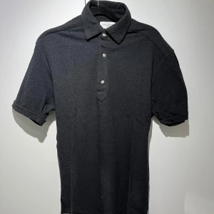 Svart pikétröja från John Henric - Snygg svart pikétröja från Polo Ralph Lauren med klassisk krage och tre knappar framtill. Perfekt för en stilren och avslappnad look. Passar bra till både jeans och chinos.