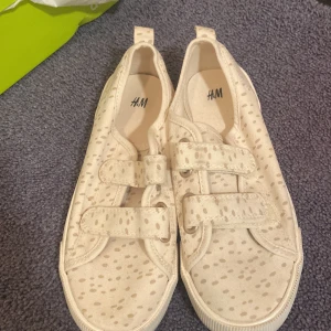 Beige sneakers från H&M - Säljer ett par beige sneakers från H&M med prickigt mönster och praktiska kardborreband. 