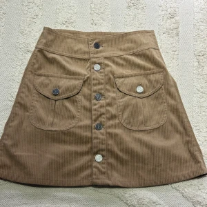 Brun/kanel manchesterkjol med knappar - Snygg brun/kanel manchesterkjol från sister point  med knappar framtill och två praktiska fickor. Är i mycket bra skick, använd knappt 2 gånger och normal i storlek. 