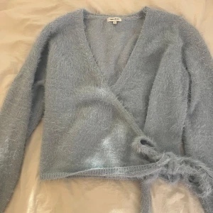 Ljusblå omlottkofta från Bubbleroom - Säljer en supermjuk ljusblå omlottkofta från Bubbleroom. Koftan har långa ärmar och knytband i midjan för en snygg passform. Perfekt för att hålla sig varm och stilren. Tillverkad i en mjuk syntetblandning. Den är storlek L men eftersom man knyter den i midjan så passar den även mig som har storlek s/xs