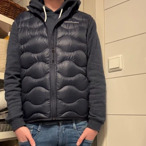 Mörkblå dunväst från Peak Performance - Säljer denna feta mörkblåa dunväst från Peak Performance med dragkedja framtill. Västen har en quiltad design som ger ett modernt utseende. Perfekt för lager-på-lager under kyligare dagar. | Storlek M passar dig mellan 170-182 | 