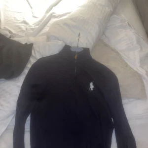 Mörkblå långärmad tröja från Ralph Lauren - Säljer en stilren svart långärmad tröja från Ralph Lauren med dragkedja vid halsen. Tröjan har det klassiska logotypbroderiet i vitt på bröstet. Perfekt för en avslappnad men snygg look.