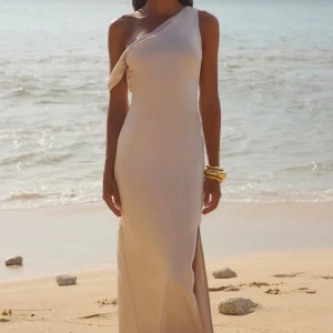 Champagnefärgad långklänning med asymmetrisk axel - Elegant champagnefärgad långklänning med en stilren oneshoulder-design och slits. Jätte fin balklänning aldrig använd bara provad. Ny pris 1200kr + frakt/ tull 600kr. Klänningen passade mig men var tyvärr för kort (jag är 177cm)