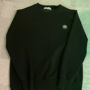 Svart tröja från Stone Island - Säljer en stilren svart tröja från Stone Island med deras ikoniska logga på bröstet. Tröjan har långa ärmar och en klassisk passform. Perfekt för en avslappnad och trendig look.