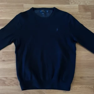 Mörkblå tröja från Ralph Lauren - Säljer en stilren mörkblå tröja från Ralph Lauren i bomull. Tröjan har långa ärmar och en diskret logga broderad på bröstet. Perfekt för en klassisk och tidlös look.