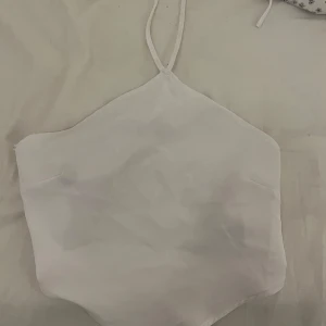 Vit topp - Säljer vit topp, oanvänd. Det finns två band som ligger bakom som man ska ha på ryggen och sedan ett (som syns) runt halsen.