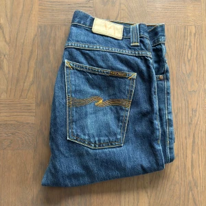 Mörkblåa Nudie Jeans - Säljer ett par mörkblåa Nudie Jeans i modellen "Grim Tim", storlek W32 L34. Tillverkade i 100% bomull med en rak passform, vilket ger en stilren och bekväm look. Jeansen är i ett bra skick och är i väldig bra skick. Nypris 1600 kr.