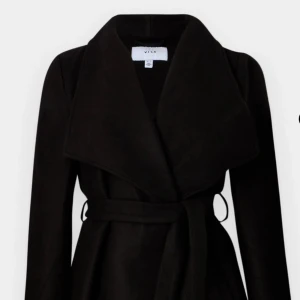 Svart kappa från VILA - Elegant svart kappa från VILA med ett stilrent bälte i midjan. Den har en klassisk design med långa ärmar och en bred krage som ger en sofistikerad look. Perfekt för kyligare dagar. Skriv privat för flera bilder. OBS bandet på kappan är borta och den är lite nopprig