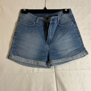 Blå jeansshorts från Denim is Dead - Snygga blå jeansshorts från Denim is Dead med klassisk femficksdesign och uppvikta benslut. Perfekta för en avslappnad stil. Midjan är normalhög och shortsen har en bekväm passform. S/M