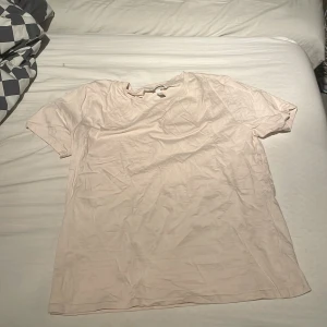 Ljusrosa t-shirt - Säljer en ljusrosa t-shirt i bomull. Den har en enkel design med korta ärmar och rund hals. Perfekt för en avslappnad stil. Passar bra till jeans eller shorts.