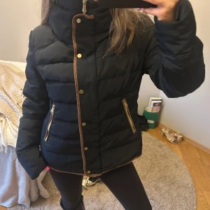 Svart dunjacka med bruna detaljer - Snygg dunjacka med en hög krage, perfekt för kyliga dagar! Storlek M men passar mig som har S🫶