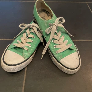 Gröna sneakers med snörning - Säljer ett par gröna sneakers med vita snören och vit sula. Skorna har en klassisk design med snörning och rund tå. Perfekta för en avslappnad stil.